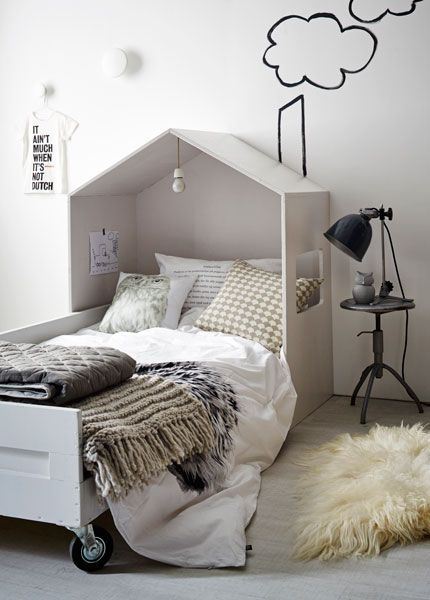 Łóżko z daszkiem na kółkach,industrialny czarny stołek z lampką i czarne graffiti na białej ścianie w pokoju dla dziecka