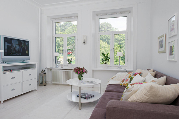 Beżowa sofa z białym okragłym stolikiem i biała komoda w salonie skandynawskim