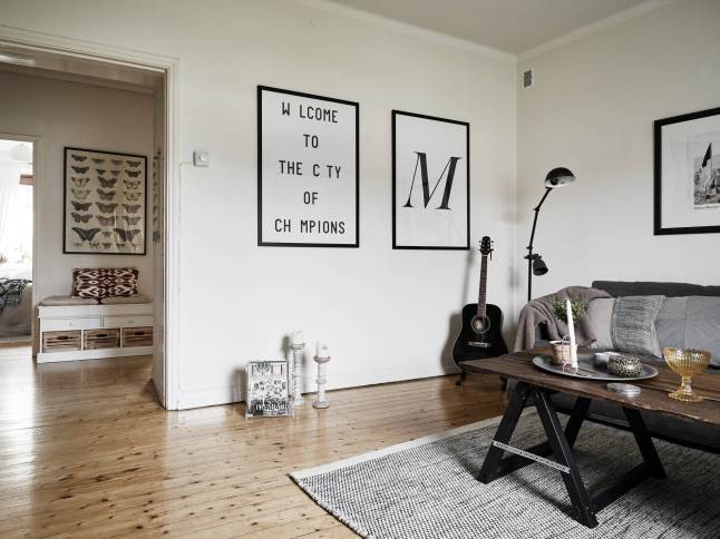 Plakaty, typografie,drewniana ława szara ze szklanym blatem i szara sofa z szarym dywanem w salonie