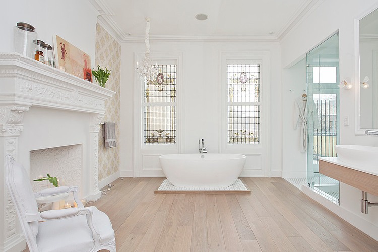 Biały pokój kąpielowy ze stylowym kominkiem,owalną wanną i drewniana podłogą