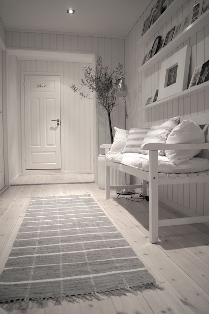 Bielone deski na podłodze w wąskim przedpokoju z drewnianą białą ławką i półkami