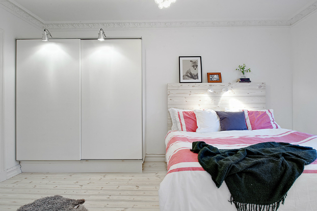 Aranżacja białej sypialni z łóżkiem z drewnianym wezgłowiem z białych desek
