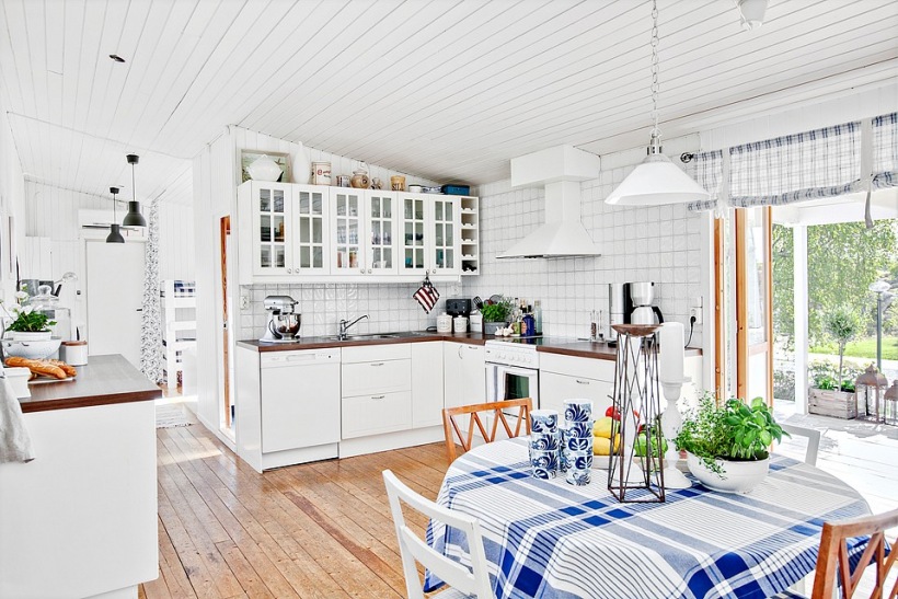 Biała kuchnia skandynawska z drewnianymi blatami, biały okap kuchenny i i okragły stół z różnymi krzesłami