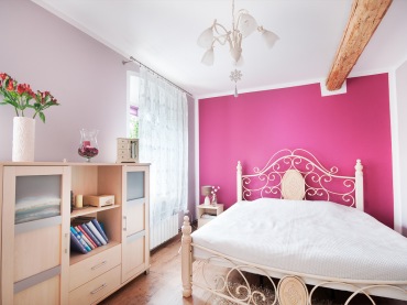 Bardzo ciekawa aranżacja sypialni, w której główną uwagę przykuwa do siebie ściana w intensywnym malinowym kolorze. Romantyczna rama łóżka kojarzy się z prowansalskim klimatem i podkreśla subtelny charakter...