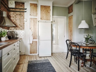 Jasne drewniane szafki i podłoga przy białej kuchni i zielonkawych ścianach dodaja przytulności.