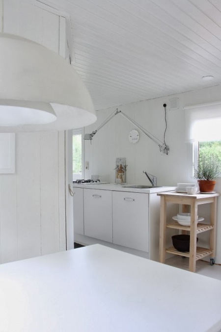 Drewniany pomocnik wyspa w bialej minimalistycznej kuchni z długim kinkietem