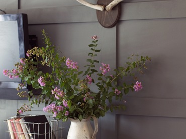 Stylowo udekorowana ściana ze stylową komodą w rustykalnym stylu. Do tego koszyki i piękny wazon z kwiatami. 