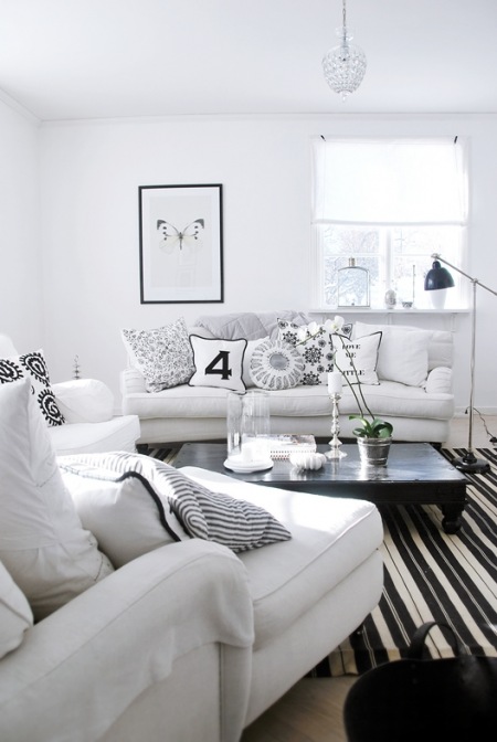 Białe sofy, fotele i  dywan w paski w salonie