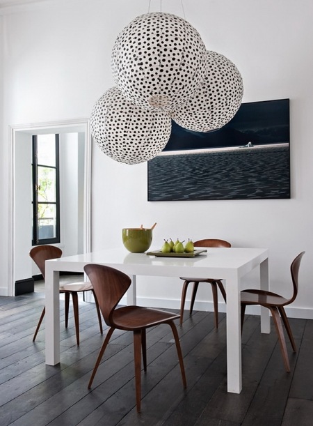 Ciemno-szara deska na podlodze,biale ściany,biały nowoczesny stół  z brązowymi krzesłami,nowoczesny obraz i papierowe kule lampiony w czarne kropki w jadalni