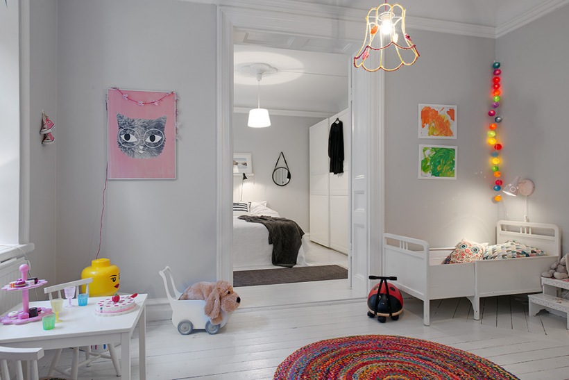 Pokój dziecięcy z białym łóżeczkiem,dzierganym okrągłym dywanem i dekoracyjnym oświetleniem z kolorowych kul