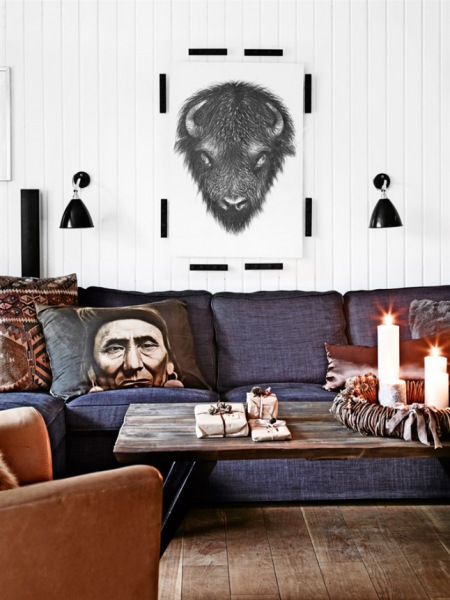 Skandynawskie grafiki,czarne kinkiety na białej ścianie nad szarą sofą z etnicznymi poduszkami