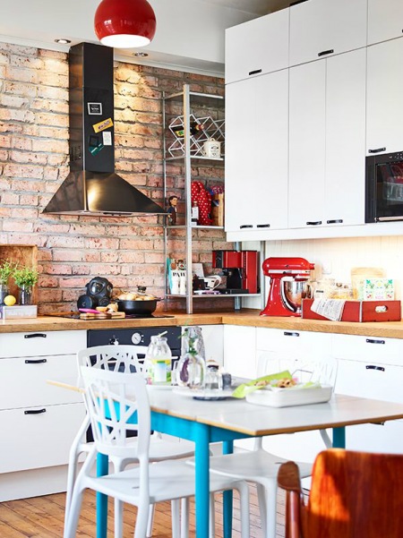 Czarny stalowy okap,czerwona cegła na ścianie,niebieski stół i białe szafki kuchenne