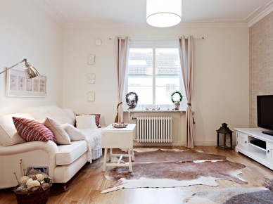 Biała sofa,zasłony,drewniany stolik kawowy i bydlęca skóra na podłodze w salonie (21921)
