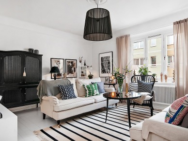 Czarna stylowa komoda z nadstawką,biały dywan w czarne paski,czarny stolik kawowy,graficzne wzory dekoracyjnych poduszek na jasnoszarej sofie w salonie (26702)