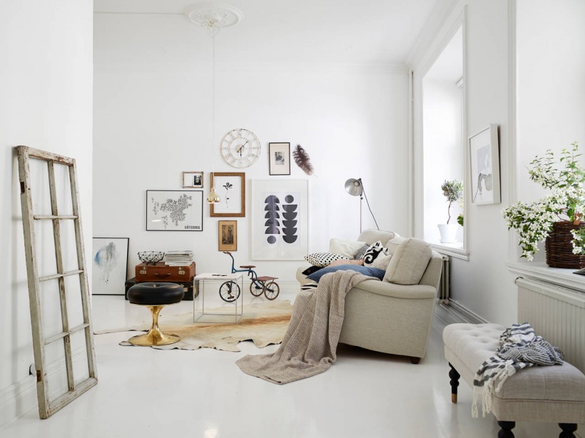 Skandynawskie grafiki,mapy i fotografie vintage w aranżacji białego salonu z dywanem ze skóry,pikowaną ławką i biała stylową sofą