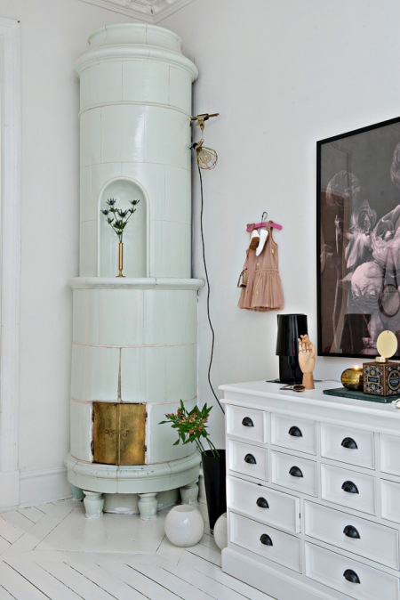 Okrągły ceramiczny piec skandynawski, biała komoda z szufladkami i nowoczesna grafika na ścianie w salonie