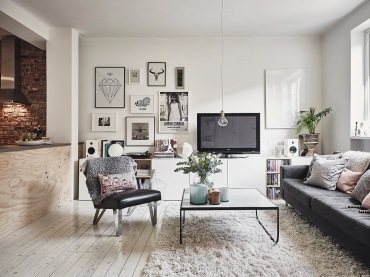 Metalowy stolik kawowy,czarny fotel na metalowych nóżkach,grafitowa sofa,białe szafki TV z galerią grafik na białej ścianie (47739)