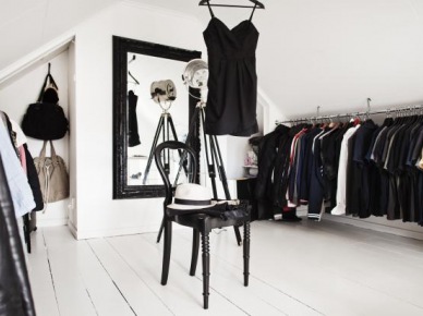 Czarne stylowe lustro na białej ścianie w garderobie z odkrytymi wieszakami,czarne giete krzesło na białych deskach podłogi (26348)