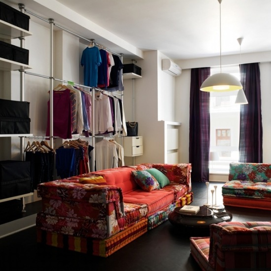 Otwarta garderoba na ścianie w salonie z kolorowymi sofami w stylu bohemy