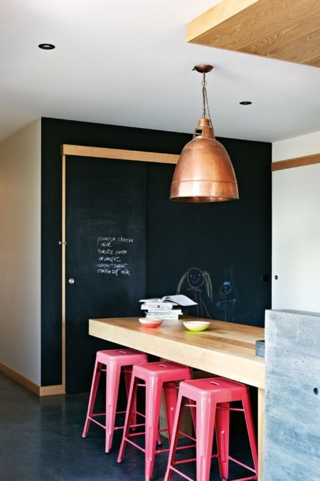 Różowe wysokie stołki przy drewnianej ladzie w kuchni z czarną ścianą z farby tablicowej
