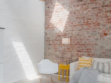 Ściana z cegły czerwonej  i pomalowanej na biało w aranżacji salonu z żółtymi dekoracjami ,krzesłem na płozach i ażurową lampą (24578)