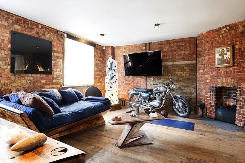 Oryginalny salon z motocyklem, dizjnerską sofą z drewna i szafirową tapicerką i ścianami z czerwonych cegieł