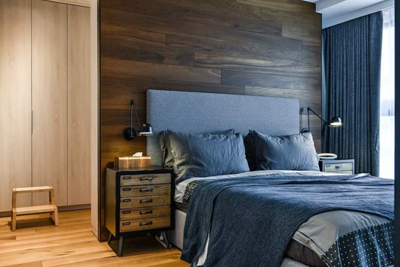 Drewniana ściana i szare łóżko z materiałowym wezgłowiem w sypialni