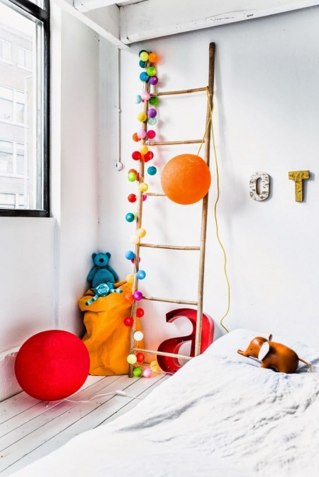 Kolorowe pomponiki i kule na drewnianej drabinie dekoracyjnej w pokoju dziecięcym