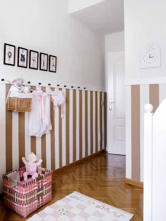 Biało-brązowa lamperia w pasy i wieszaczki na ścianie w pokoju dziecięcym