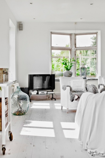 Biały salon w stylu skandynawskim z szafką na kólkach,ozdobnym słojem szklanym i białym fotelem