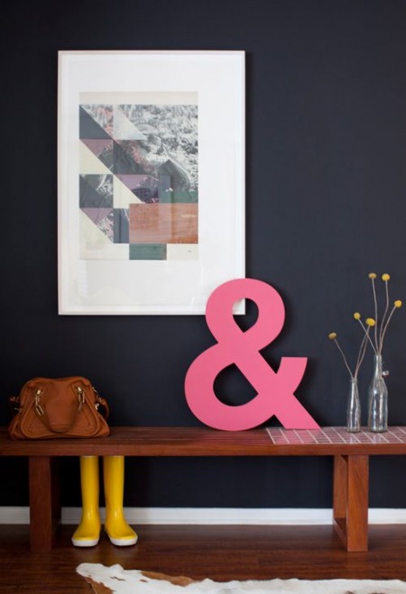 Czarna ściana,różowa litera 3d, drewniana ławka i nowoczesna grafika w dekoracji przedpokoju