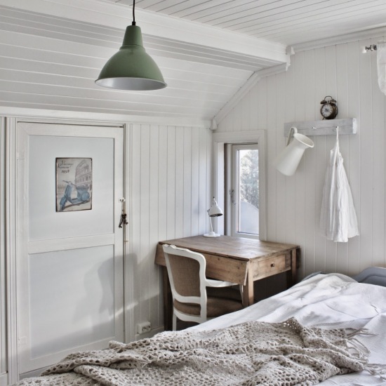 Zielona lampa metalowa,białe panele z drewna na ścianach,drewniany składany stolik i biało-brązowe krzesło francuskie w sypialni