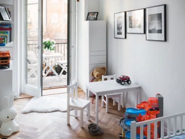 Pokój dla dziecka w stylu skandynawskim urozmaicono czarnymi dodatkami oraz zabawkami w kolorze, które wystawione są na...