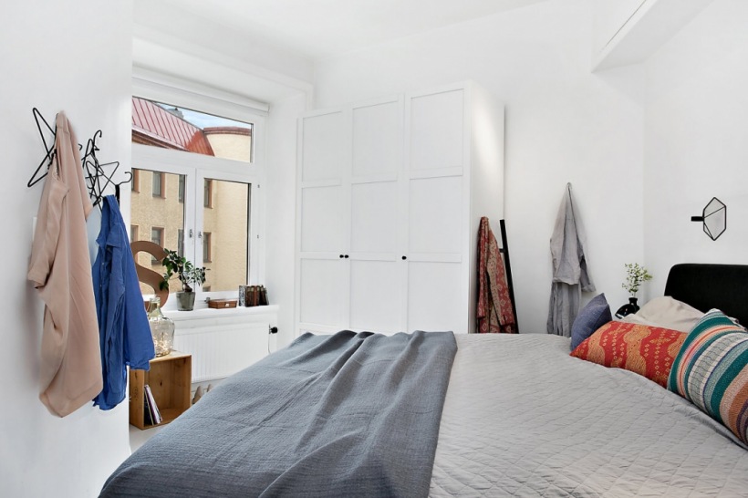 Białe szafy w sypialni z czarnym łóżkiem ubranym w szarą narzutę i kolorowe poduszki ozdobne