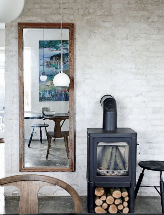 Żeliwny kominek,prostokatne lustro drewniane,ściana z surowej cegły