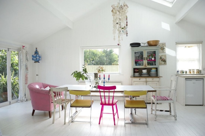 Kredens w stylu shabby i kolorowe rózne krzesła przy stole w białej jadalni