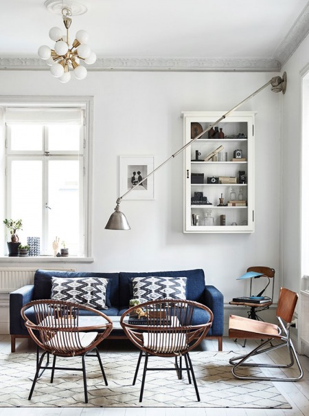 Salon w stylu vintage z ażurowymi drewnianymi fotelami, granatową sofą i kinkietem na wysięgniku