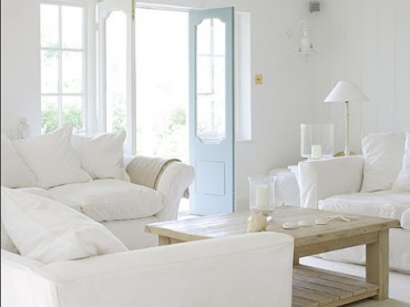 Aranżacja salonu z białymi sofami,drewnianym stolikiem ,wiklinowym koszem i niebieskimi drzwiami (21731)