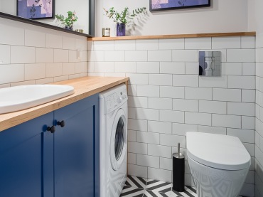 Aranżacja łazienki wygląda inspirująco. Białe ściany, niebieska szafka oraz drobne drewniane detale ładnie uzupełniają...