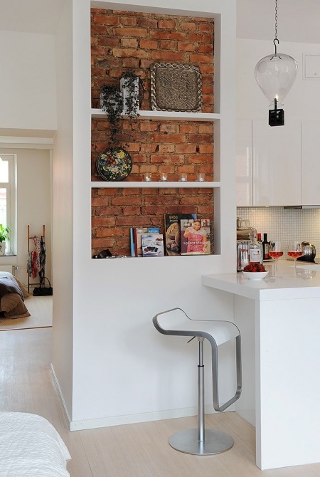 Biała zabudowa z pólkami w kuchni ze ścianą z cegły