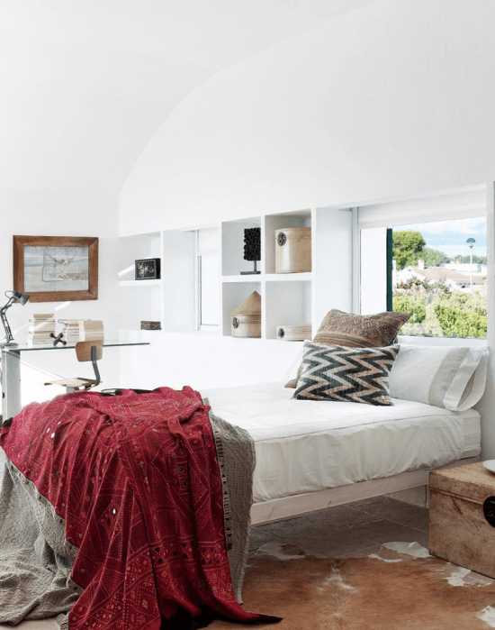 Murowane wapienne półki,drewniane lustro i łóżko,drewniana skrzynia i dywan ze skóry bydlęcej w aranżacji sypialni