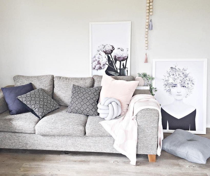Pastelowy salon z szarą sofą i czarno-białymi grafikami