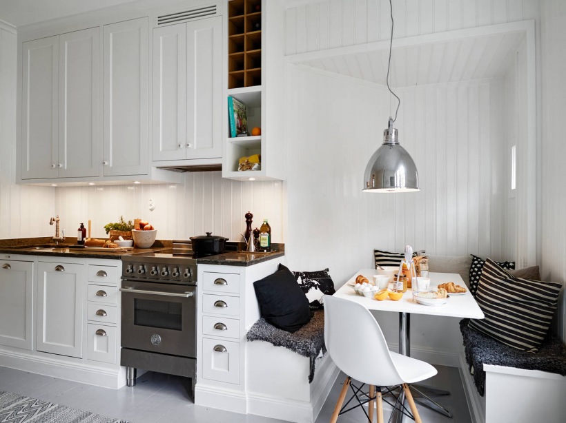 Tradycyjna biała kuchnia skandynawska z zabudowanymi siedziskami, biało-czarnymi poduszkami i srebrną lampą nad stołem