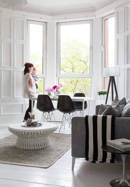 Biały nowoczesny stó z czarnymi krzesłami na metalowych nóżkach urządzony w wykuszu w salonie