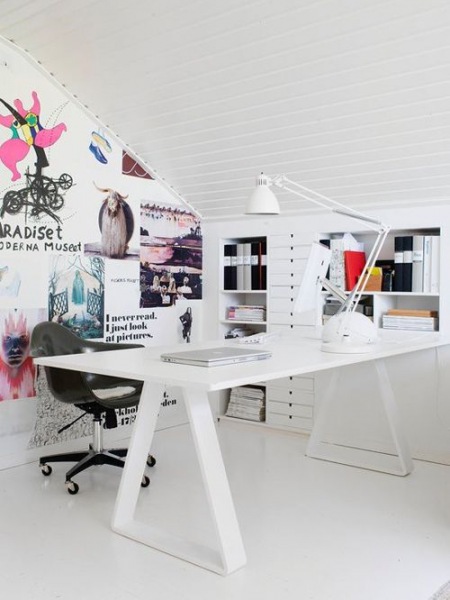 Białe biurko nowoczesne,biała lampa na biurku,biała zabudowa z pólkami i szufladami pod skośnym dachem i pomysłowa ściana z naklejonymi plakatami i napisami