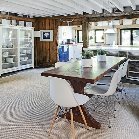 Drewniany wiejski stół,białe nowoczesne krzesła,przeszklona witryna i  deski na ścianach w  wiejskiej  kuchni z jadalnią