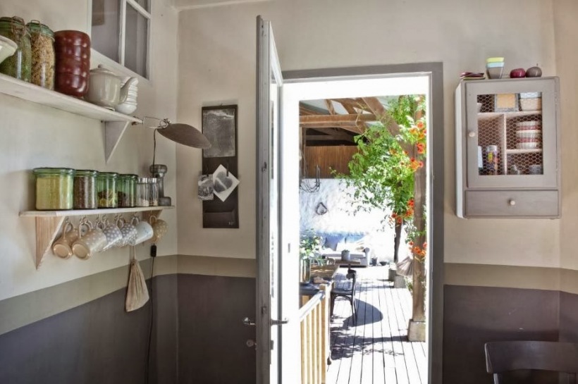 Szare lamperie na ścianach,drewniane szare szafki i białe półki w aranżacji kuchni wychodzącej na taras