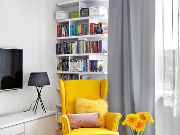 Żółty fotel wraz kolorowymi poduszkami oraz kwiatami w wazonie dominują w tym nowoczesnym, utrzymanym w stosnowanych...