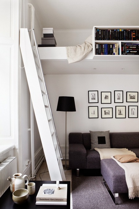 Mini antresola z półkami na książki i białą drabiną nad grafitową sofą w salonie
