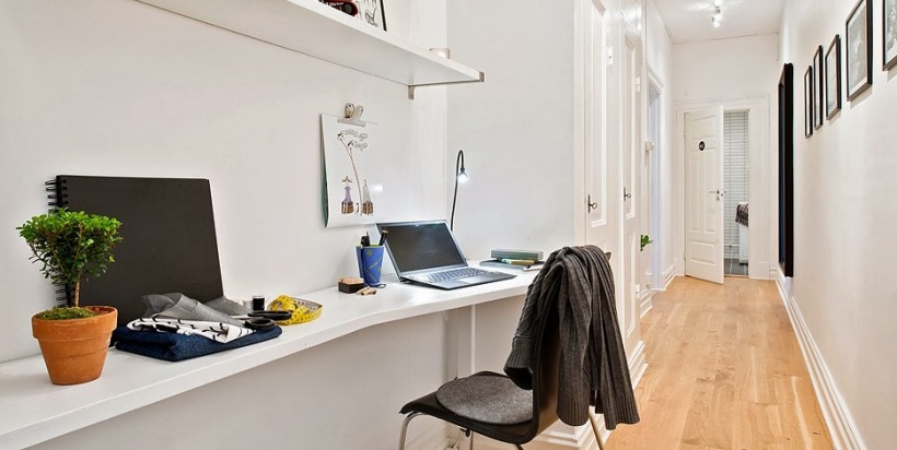 Profilowane białe wąskie półki w roli małego biurka w wąskim białym korytarzu